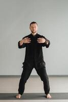 A man in black kimano practicing qigong energy exercises indoors photo