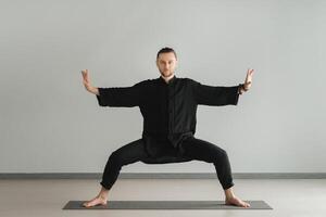 A man in black kimano practicing qigong energy exercises indoors photo