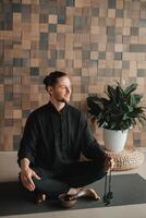 Portrait of a young man in a black kimano sitting in a lotus position on a gym mat in the interior photo