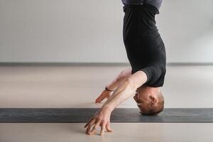 A man performs a yoga pose with support on his head in the gym. Yogi in a headstand photo