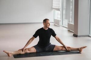 An athletically built man does yoga in the gym on a mat photo