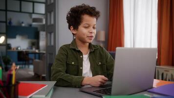 Smiling little African American boy son kid child pupil at home table talking online call conference chat distant study education e-learning internet laptop computer talk with teacher tutor video
