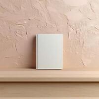 Minimalist blank book on a wooden shelf against a textured pink wall. photo
