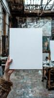 a woman hand holding up a a blank white piece of A4 paper, there is an art studio in the background, realistic photo