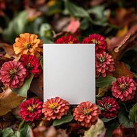 Vibrant fall flowers surround a blank white card on a colorful leaf background. photo