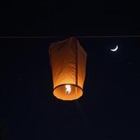 Lantern floats in night sky before crescent moon photo