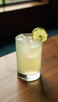Clear glass filled with a refreshing margarita drink and garnished with lime slice serves invitingly on a rustic wood table photo
