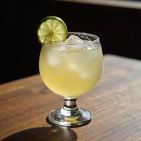 Clear glass filled with a refreshing margarita drink and garnished with lime slice serves invitingly on a rustic wood table photo