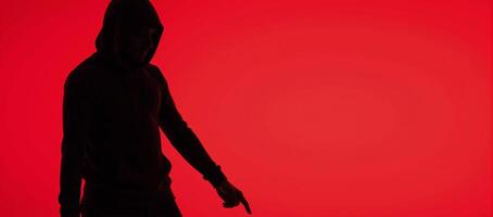 Man in hood with no visible face silhouetted against red background photo