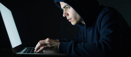 A hacker engages in cybercrime through his laptop on a dark backdrop while a young hacking prodigy battles him in an Internet Security Standoff photo