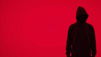 Man in hood with no visible face silhouetted against red background photo