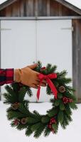 Closeup portrait of vintage leather gloves holding a festive wreath against a blurry backdrop of a snowy barn photo