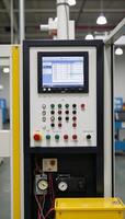 Industrial control panel within a factory showcasing rows of buttons gauges and monitors displaying data amidst metallic framing and wires photo