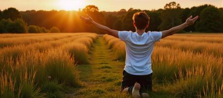 Person kneels with open arms toward sunsetbackdrop for prayer at meadow photo
