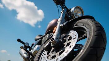 Detailed closeup image of shiny motorcycle wheel with intricate front suspension beneath a clear blue sky photo