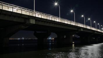 A litup city bridge showcases the glow from passing vehicles crossing during nighttime photo