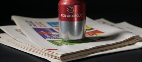 Nonalcoholic beer can labeled with text displayed atop sports newspaper stacks photo