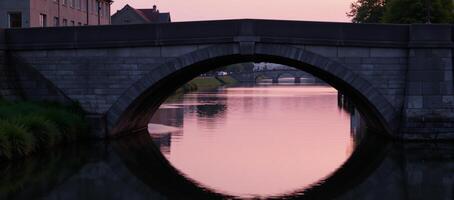 Stone bridge illuminated by soft pink light reflected on tranquil waters during twilight photo