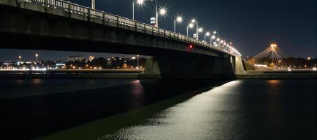 A litup city bridge showcases the glow from passing vehicles crossing during nighttime photo