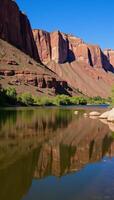 Bright sunlit day at Lees Ferry showcases the peaceful Colorado River flowing amidst Grand Canyons colorful cliffs photo