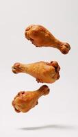 Isolated fried chicken legs suspended midair against a pure white backdrop photo