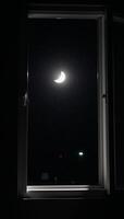 A halfmoon illuminates a dark room from an open window at night photo
