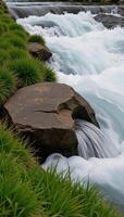 A closeup of a cascading water stream with nearby rocks and surrounding lush greenery photo