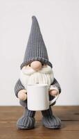 Adorable gnome figurine grayclad mugholding stands on wooded surface photo