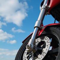 Detailed closeup image of shiny motorcycle wheel with intricate front suspension beneath a clear blue sky photo