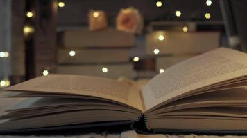 Open book with fairy lights sparkling in the background. A stack of books is blurred in the background video
