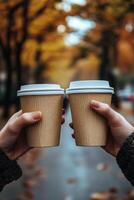 Two hands holding coffee cups while walking through an autumn park filled with colorful trees photo
