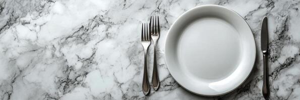 Elegant dining setup with a clean white plate and silver cutlery on a marble table photo