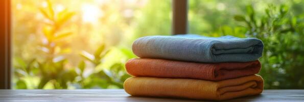 Colorful towels stacked beside a window with a garden view during golden hour light photo