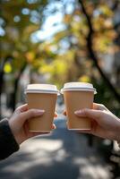 Two hands holding coffee cups while walking through an autumn park filled with colorful trees photo