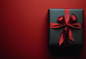 A beautifully wrapped black gift box with a red ribbon on a vibrant red backdrop photo
