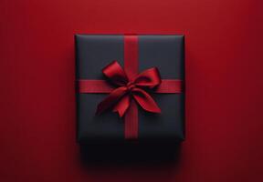 A beautifully wrapped black gift box with a red ribbon on a vibrant red backdrop photo