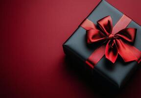 A beautifully wrapped black gift box with a red ribbon on a textured red and black background photo