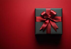 A beautifully wrapped black gift box with a red ribbon on a vibrant red backdrop photo