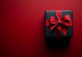 A beautifully wrapped black gift box with a red ribbon on a textured red and black background photo