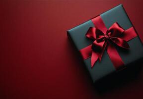 A beautifully wrapped black gift box with a red ribbon on a textured red and black background photo