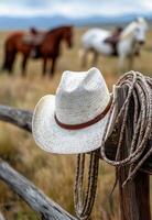 A cowboy hat rests on a wooden fence in a peaceful pasture with grazing horses in the background photo
