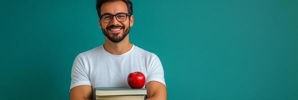 Young man with glasses holding books and an apple against a teal background photo