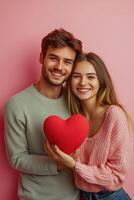 Young couple poses together with a heart shaped object against a pink backdrop photo