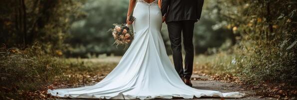Elegant wedding couple walking hand in hand along a serene, tree lined path during golden hour photo