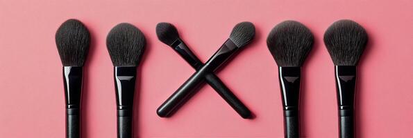 A set of makeup brushes in varying shapes on a pink background photo