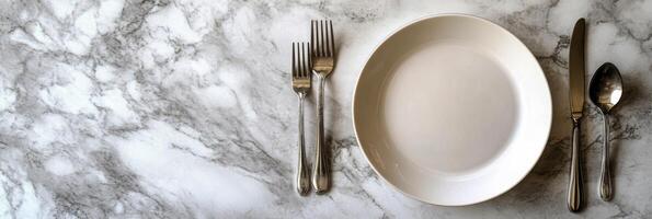 Elegant dining setup with a clean white plate and silver cutlery on a marble table photo