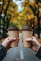 Two hands holding coffee cups while walking through an autumn park filled with colorful trees photo
