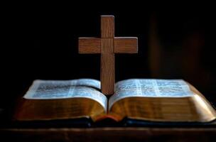 A wooden cross stands on an open Bible in a dimly lit room during evening hours photo