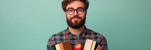 Young man with glasses holding books and an apple against a teal background photo