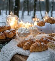 Cozy winter picnic with croissants and marshmallows in a snowy forest setting at dusk photo